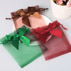 Three elegant organza drawstring gift bags in shades of brown, pink, and red are displayed on a light surface.