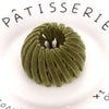 A close-up of a green velvet horsetail hair clip resting on a white plate with black text.