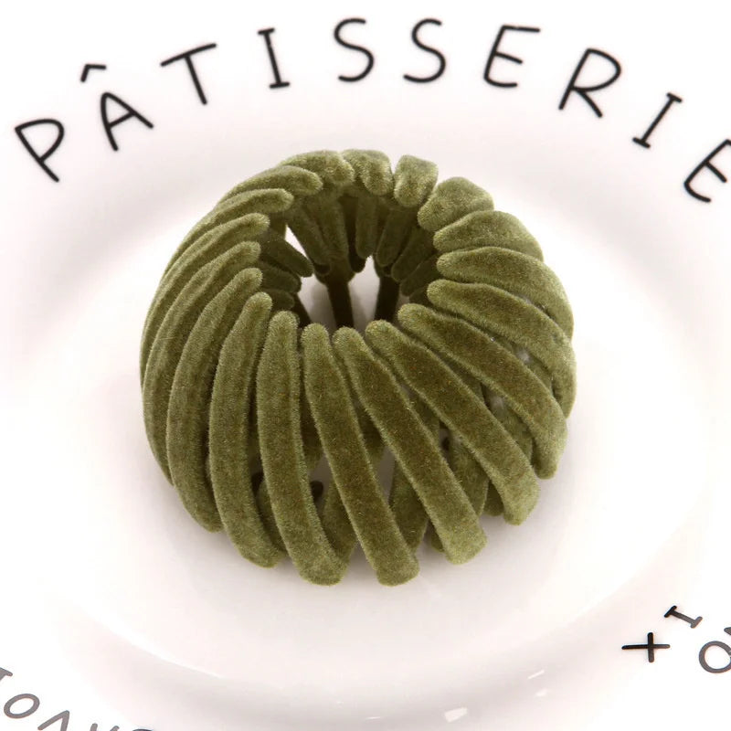A close-up of a green velvet horsetail hair clip resting on a white plate with black text.