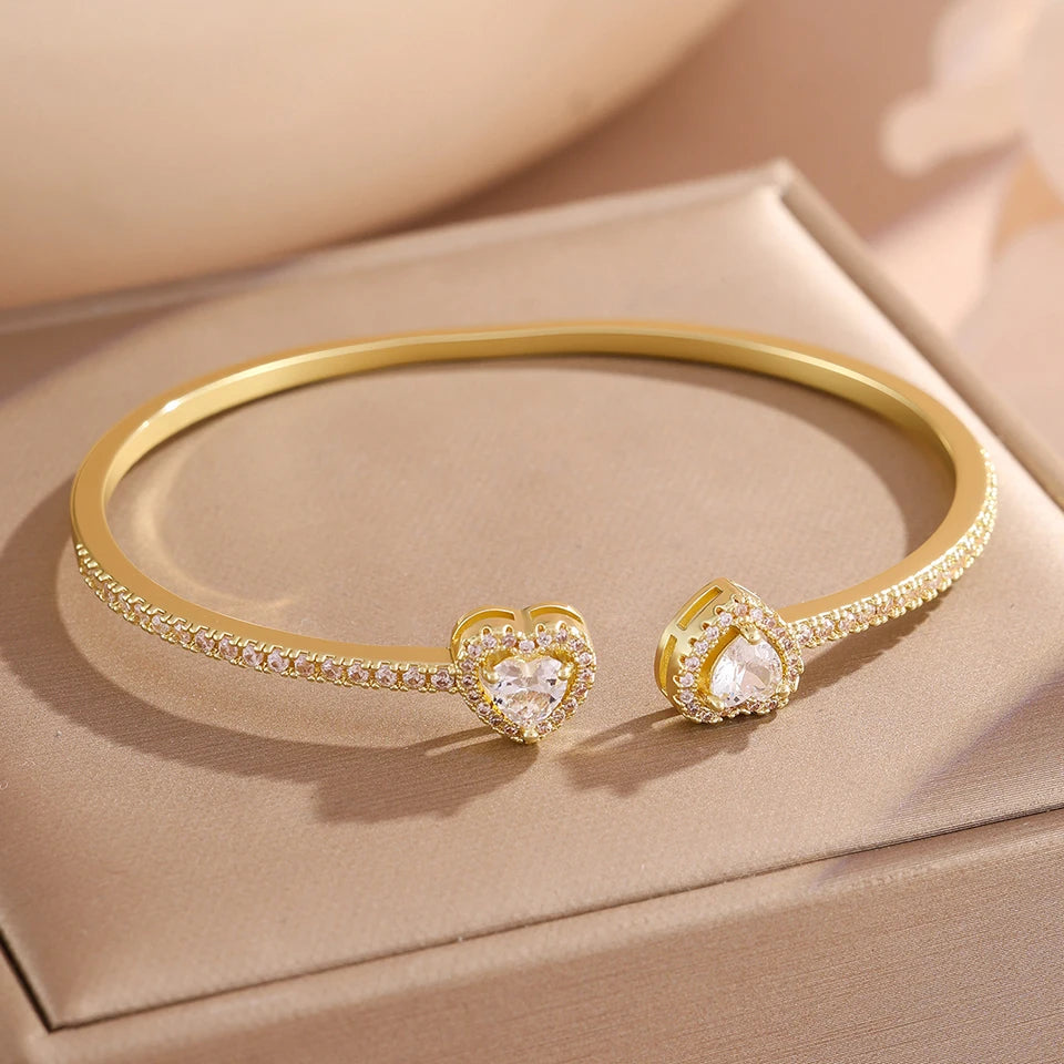 A set of gold-toned stacking bracelets featuring heart-shaped charms encrusted with clear rhinestones.