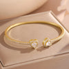 A set of gold-toned stacking bracelets featuring heart-shaped charms encrusted with clear rhinestones.