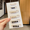 A display of gold-toned pearl and black bead brooch pins arranged on a white card.