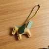A tan horse pendant charm with green accents is displayed on a wooden surface.