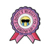A lapel pin featuring a purple and pink rosette with the text Don't Want I Don't Grow Up