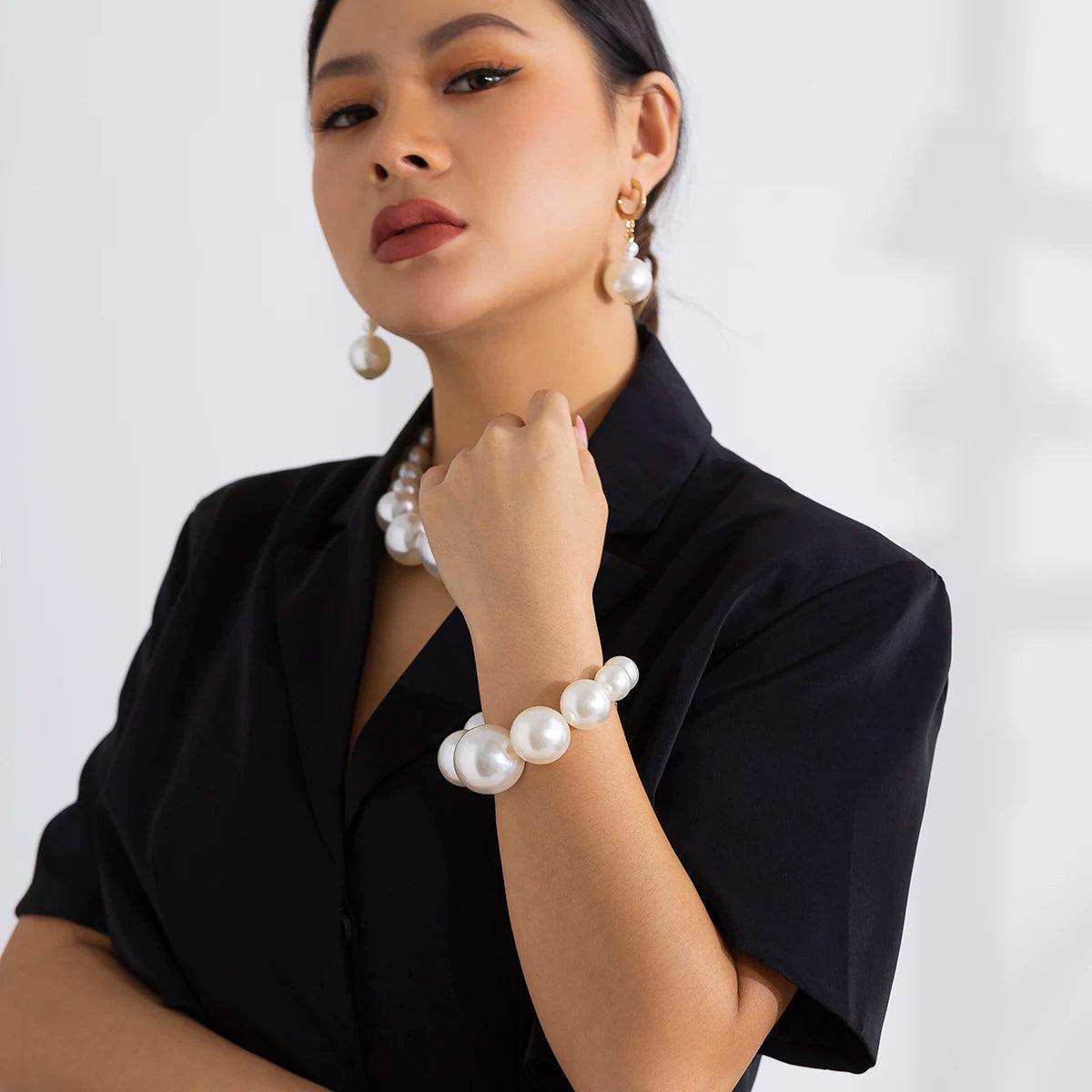 Une femme portant une chemise noire à col et des bijoux de perles, y compris un collier ras-du-cou et un bracelet.