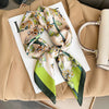 A silk scarf tied in a bow featuring floral patterns in shades of orange, green, and cream, displayed on a beige blazer.