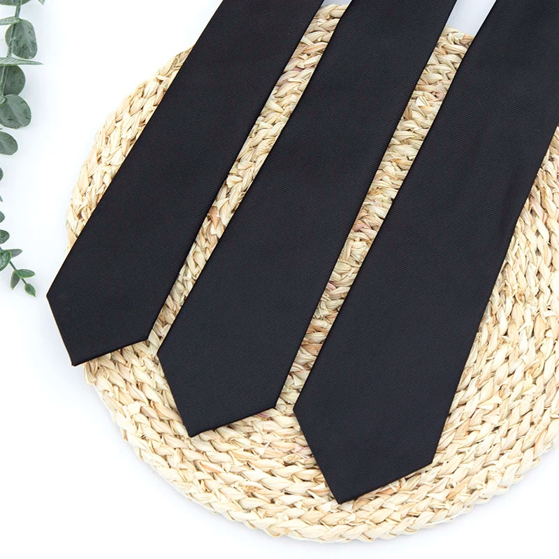 Three black neckties laid diagonally on a woven straw mat.