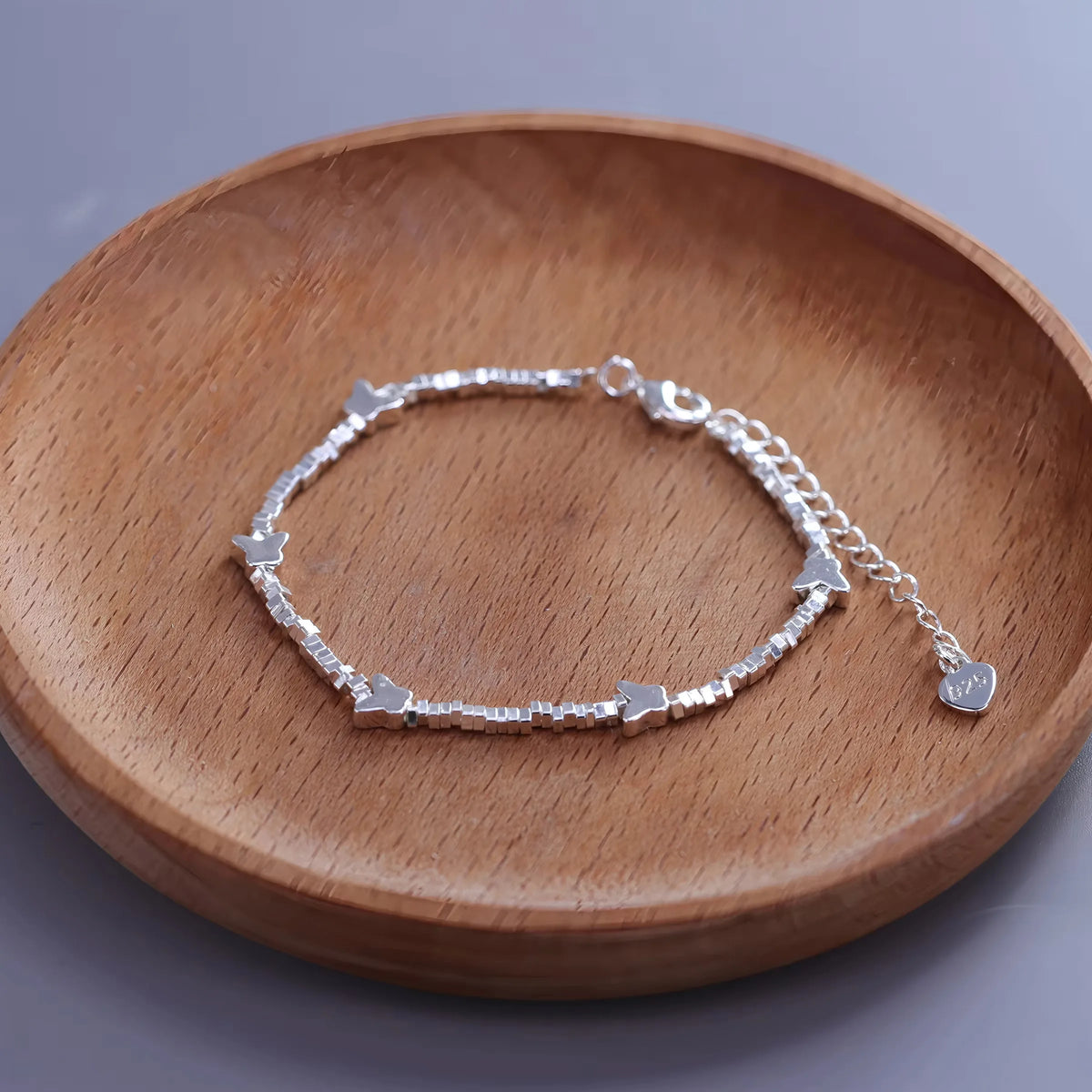 Sterling silver double heart charm bracelet displayed on a wooden dish