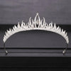 A sparkling crystal bridal crown with pointed petals and a central jewel displayed on a dark surface.