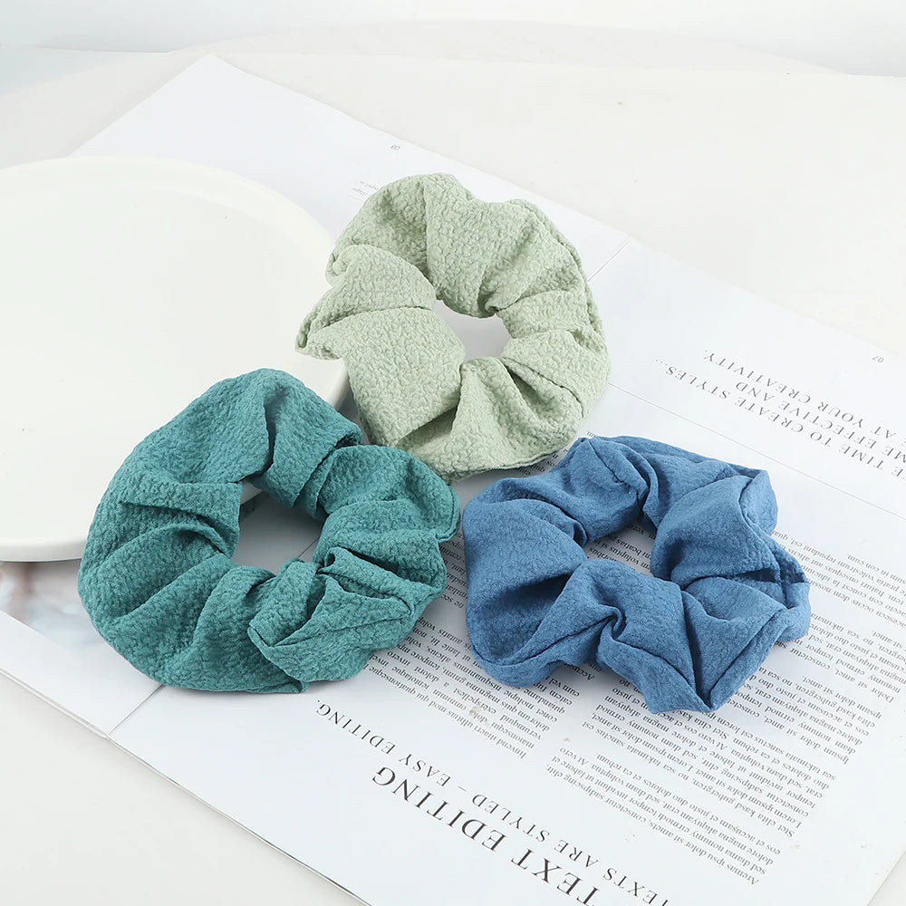 Three knitted hair scrunchie headbands in shades of sage green, teal, and dusty blue displayed on a white paper.