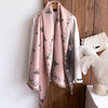 A pink pashmina shawl with a floral print is displayed hanging on a wooden hanger against a light wall.