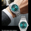 A close-up of a stainless steel watch with a dark green dial on a wrist, showcasing sharp lines and a refined look.