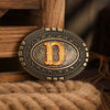 A vintage western belt buckle with an ornate design and gold tone resting on a wooden surface.