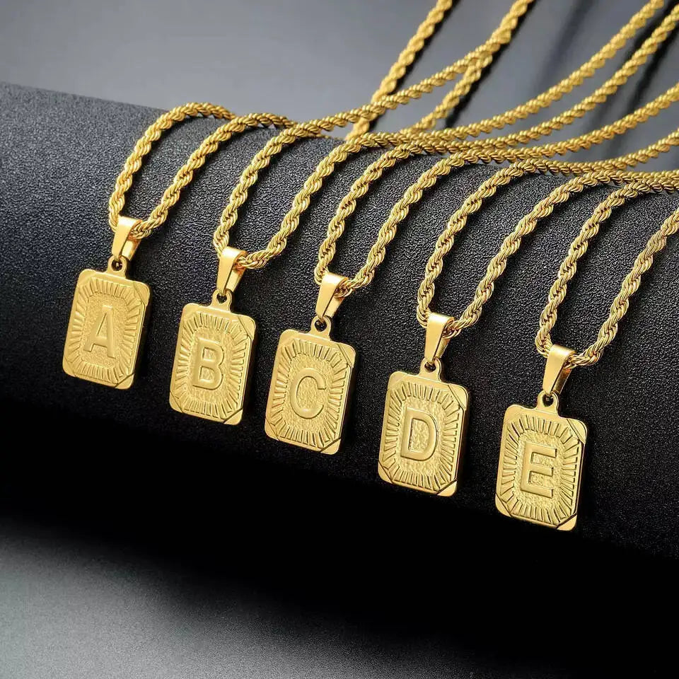 A set of five gold-plated letter pendant necklaces labeled A through E displayed on a dark surface.