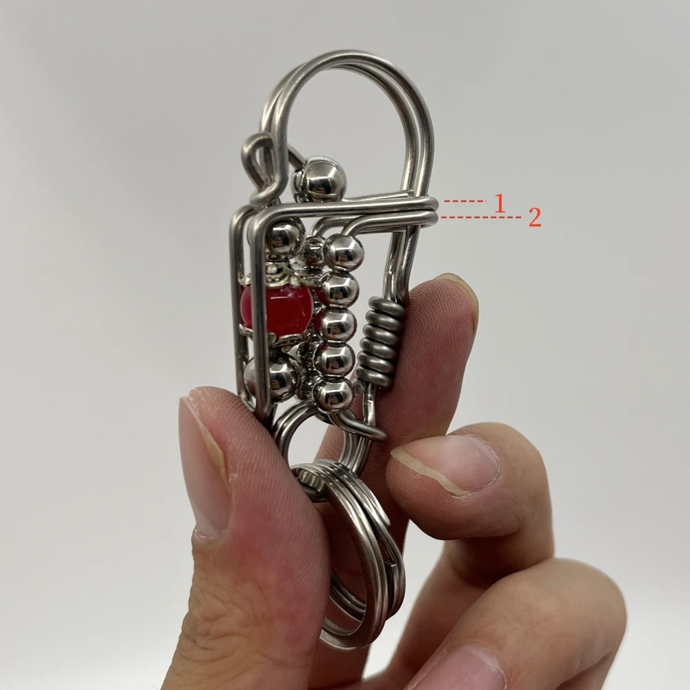 Une main tient une clé USB mécanique en acier inoxydable avec une perle rouge et un fil enroulé.