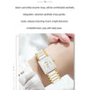 A close-up of a gold and white ceramic fashion wristwatch worn on a wrist, with a white lace garment in the background.