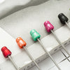 A collection of beadable ballpoint pens in various colors, including pink, green, and red, resting on a light gray surface.