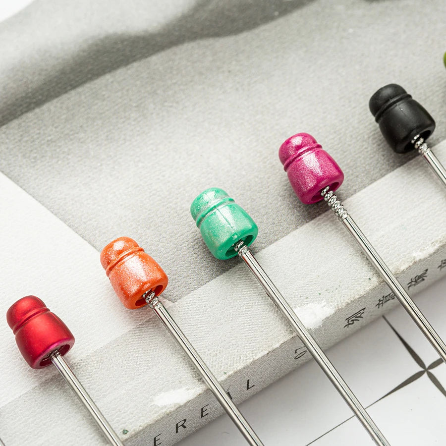 A collection of beadable ballpoint pens in various colors, including pink, green, and red, resting on a light gray surface.