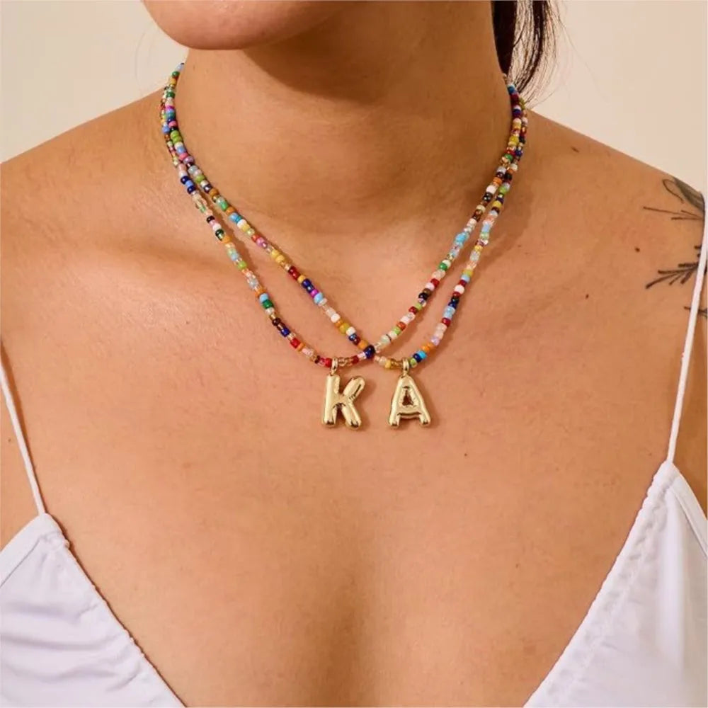 Collar de cuentas multicolor con dije inicial usado alrededor del cuello.