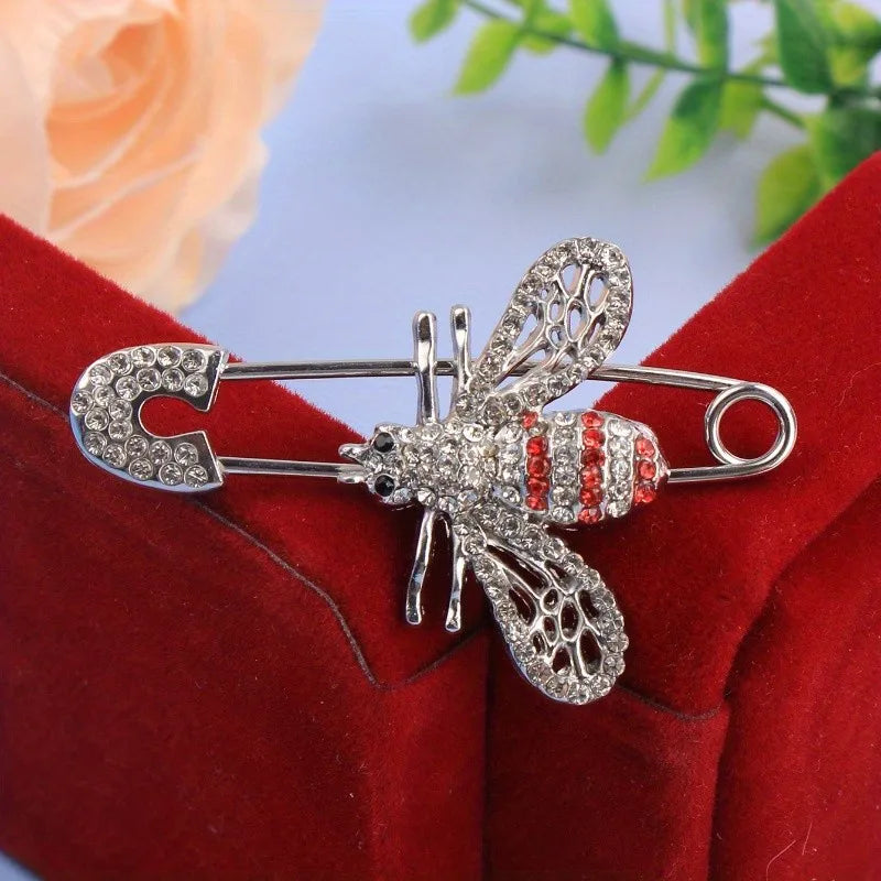 Broche en argent avec un détail d'abeille et d'insecte, ornés de pierres claires sur fond de velours rouge.