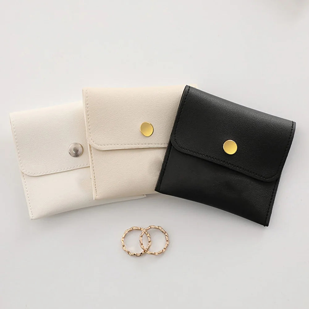 A pair of elegant PU leather jewelry pouches in cream and black with gold snap buttons.