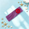 Un bandeau pour cheveux rayé rose et vert sur une surface bleu clair entourée d'étoiles de mer et de coquillages.