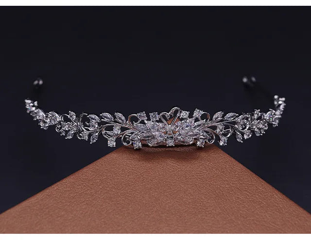A sparkling cubic zirconia bridal tiara headband displayed on a brown surface.