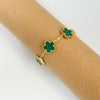 Gold plated stainless steel double-sided petal bracelet with green enamel petals on a brown textured background