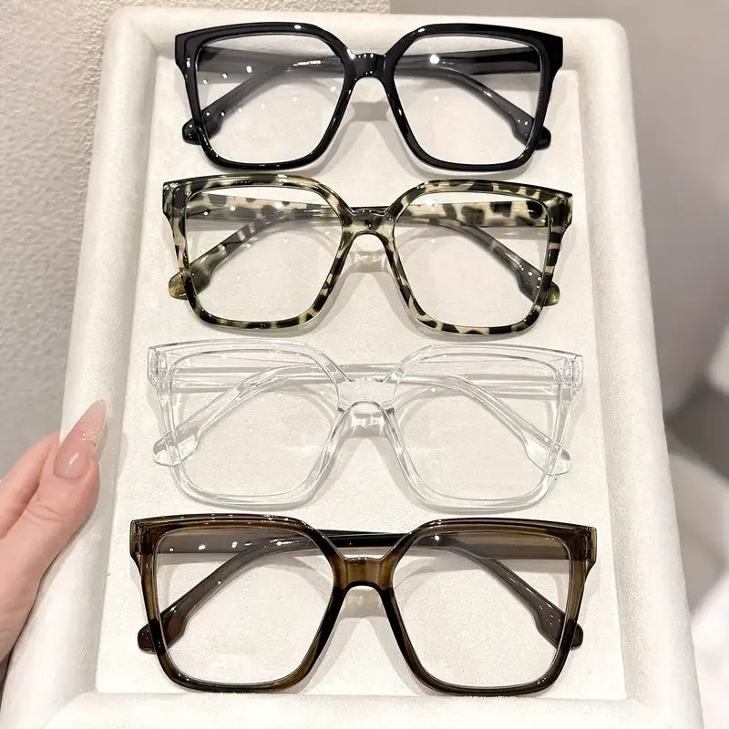 A display of four pairs of elegant geometric reading glasses with various colored frames and transparent lenses.