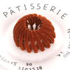 A circular arrangement of brown, textured hair clips resembling horsetail braids on a white plate.