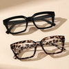 A pair of black, thick-framed reading glasses with a dark gray lens resting on a light surface.