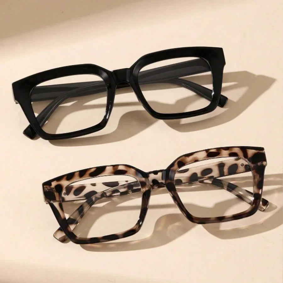 A pair of black, thick-framed reading glasses with a dark gray lens resting on a light surface.