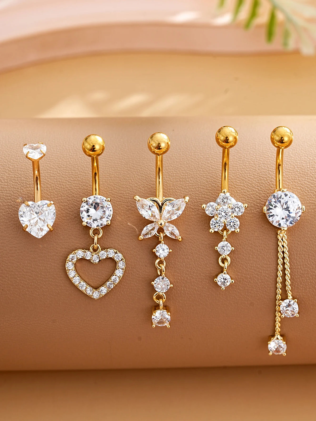 A set of five gold stainless steel dangled belly button rings featuring clear and white stones.