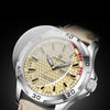 A silver watch with a gold-toned face and a light brown leather strap, featuring synthetic sapphire glass.