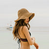 A woman wearing a hand-woven straw visor hat while standing near the water.