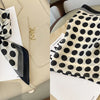 A black and white polka dot silk scarf tied in a bow, displayed on a light beige surface.