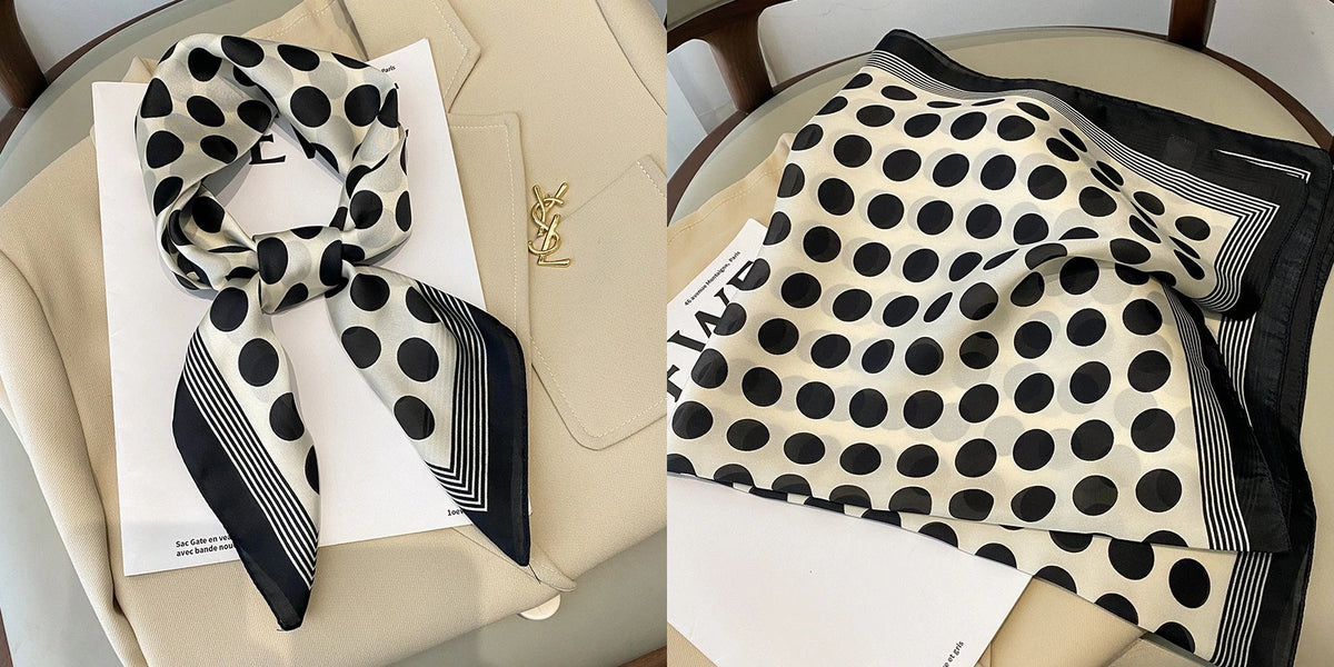 A black and white polka dot silk scarf tied in a bow, displayed on a light beige surface.