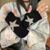 Una persona vistiendo ropa beige sostiene guantes sin dedos de punto negros con patrones de estrellas.