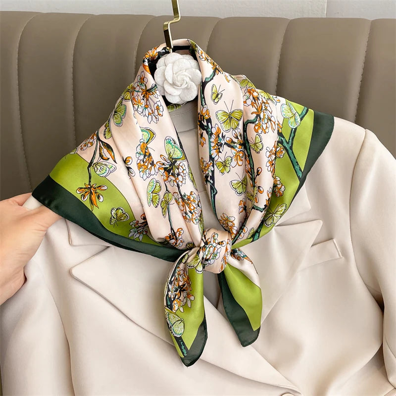 A silk scarf featuring a floral pattern in peach and green tones tied as a square shawl on a hanger.
