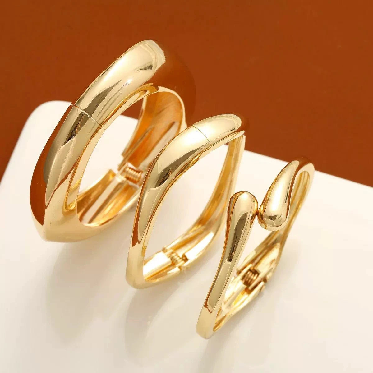 A set of gold chunky cuff bangle bracelets displayed on a white surface.