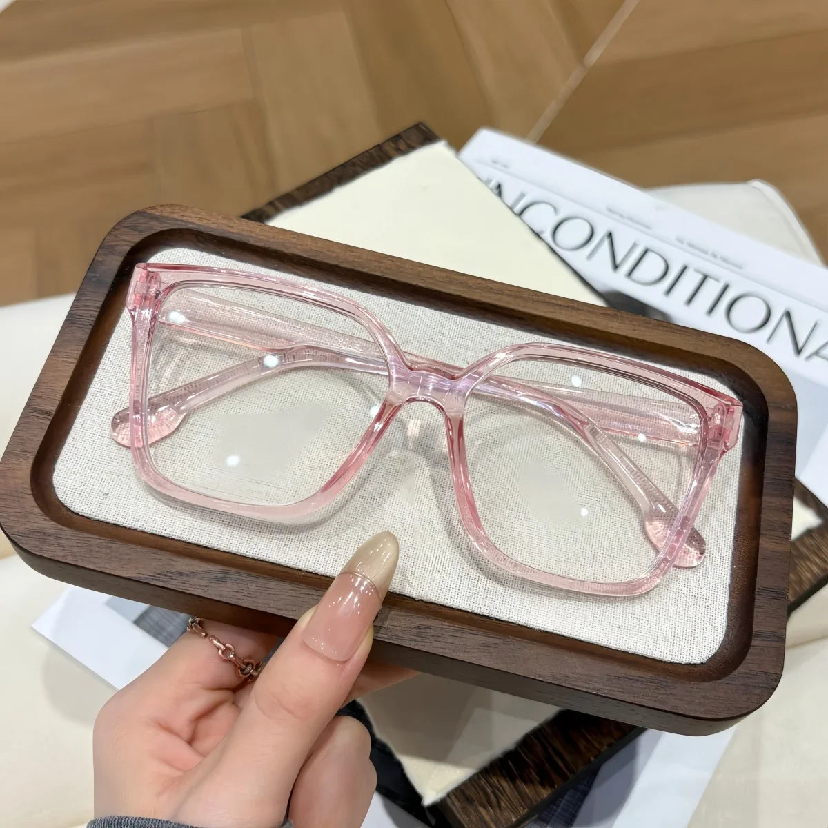 A pair of pink geometric reading glasses with transparent lenses resting on a wooden tray.