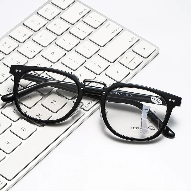 A pair of black-framed multifocal reading glasses resting on a white laptop keyboard.