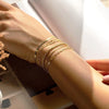A hand wearing a stack of dainty gold plated bracelets on the wrist.