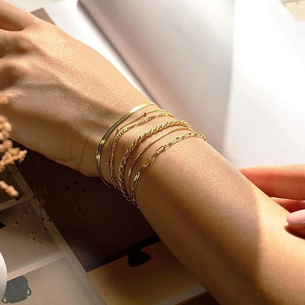 A hand wearing a stack of dainty gold plated bracelets on the wrist.