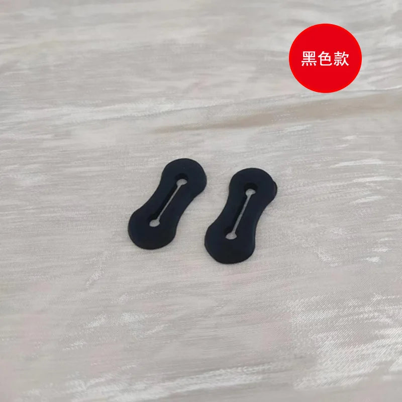 Dos hebillas ajustables para mangas de camisa negras sobre una superficie de madera blanca.