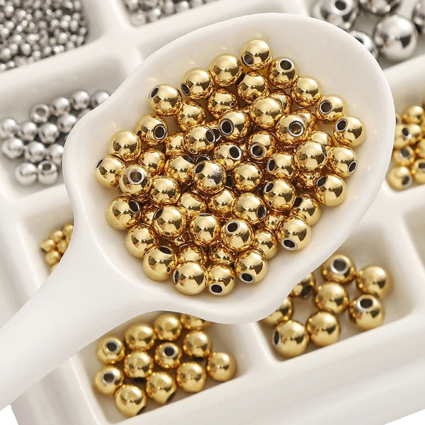 A white silicone spatula holds a pile of gold-colored stainless steel spacer beads for DIY jewelry making.