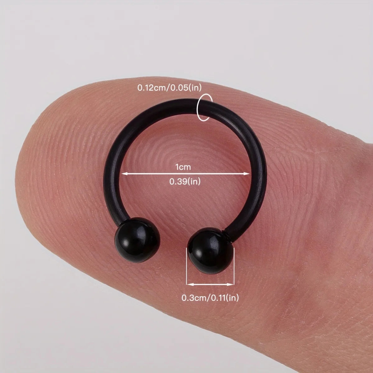 A black flexible acrylic piercing jewelry set with a hoop and two bead-like components shown on a finger.