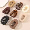 A collection of matte oval hair claw clips in various shades and leopard print patterns arranged on a light surface.