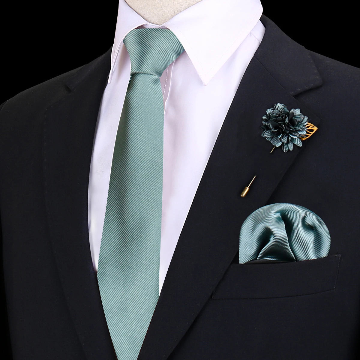 Chaqueta negra con camisa rosa claro, corbata de seda verde salvia y un prendido floral oscuro en la solapa.