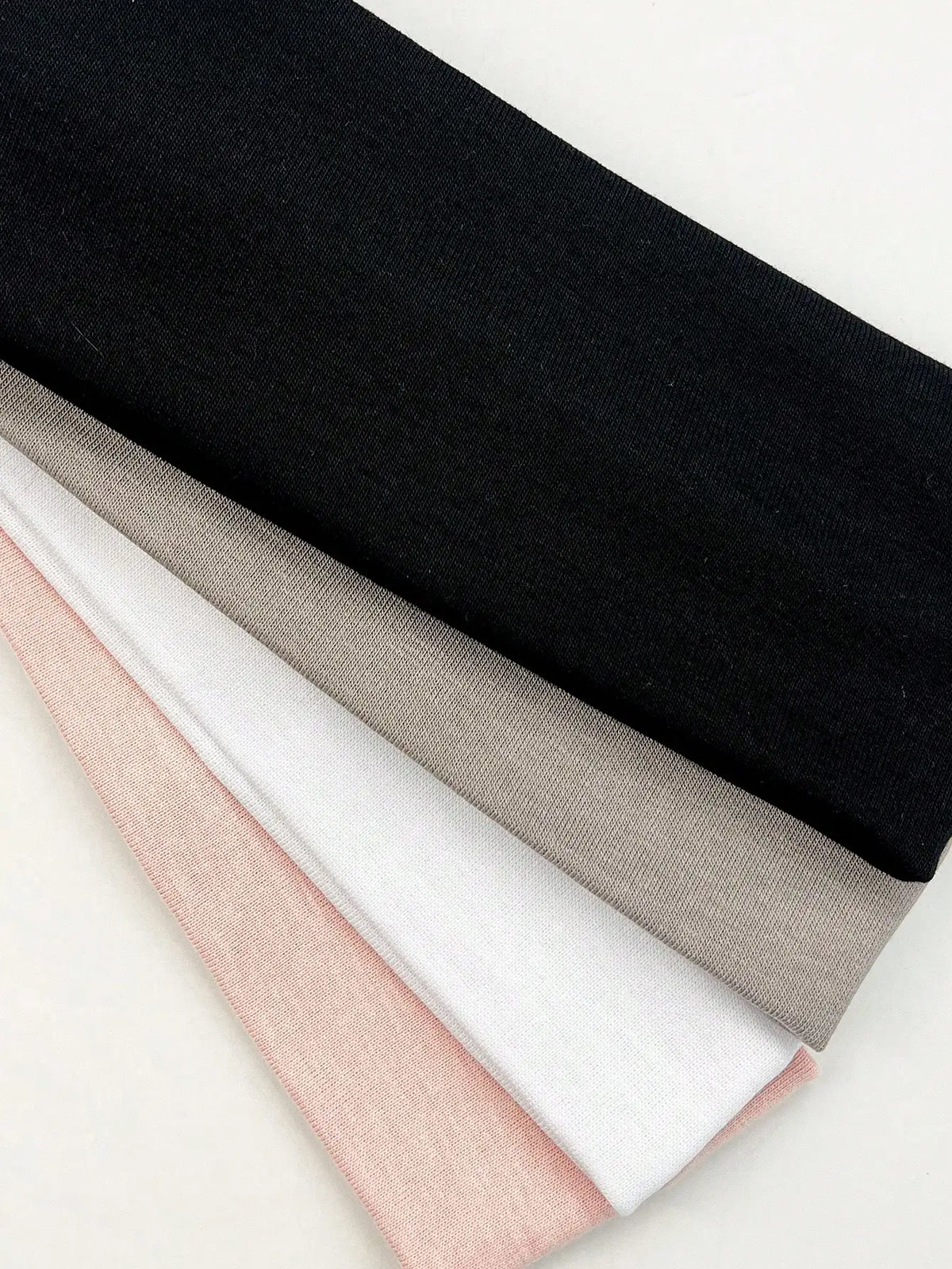 A stack of four knitted hair bands in black, gray, white, and pink shades.
